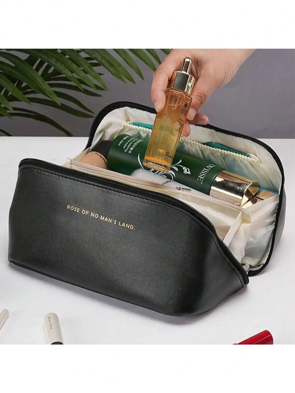 A black leather travel makeup organizer bag is open, showing a gold perfume bottle and other cosmetics inside.
