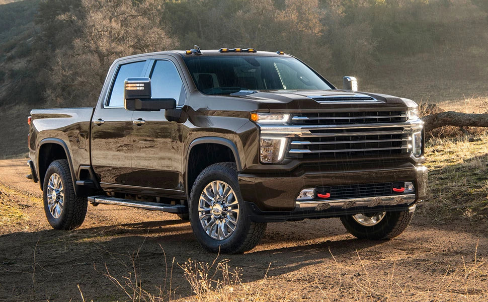 A dark brown Chevy Silverado pickup truck with tow hook covers parked on a dirt road.