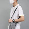 A person wearing a black cap and face mask holds a gray mini crossbody phone bag with an adjustable strap.