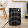 A black and white checkered fabric laundry basket with handles sitting on a wooden floor.