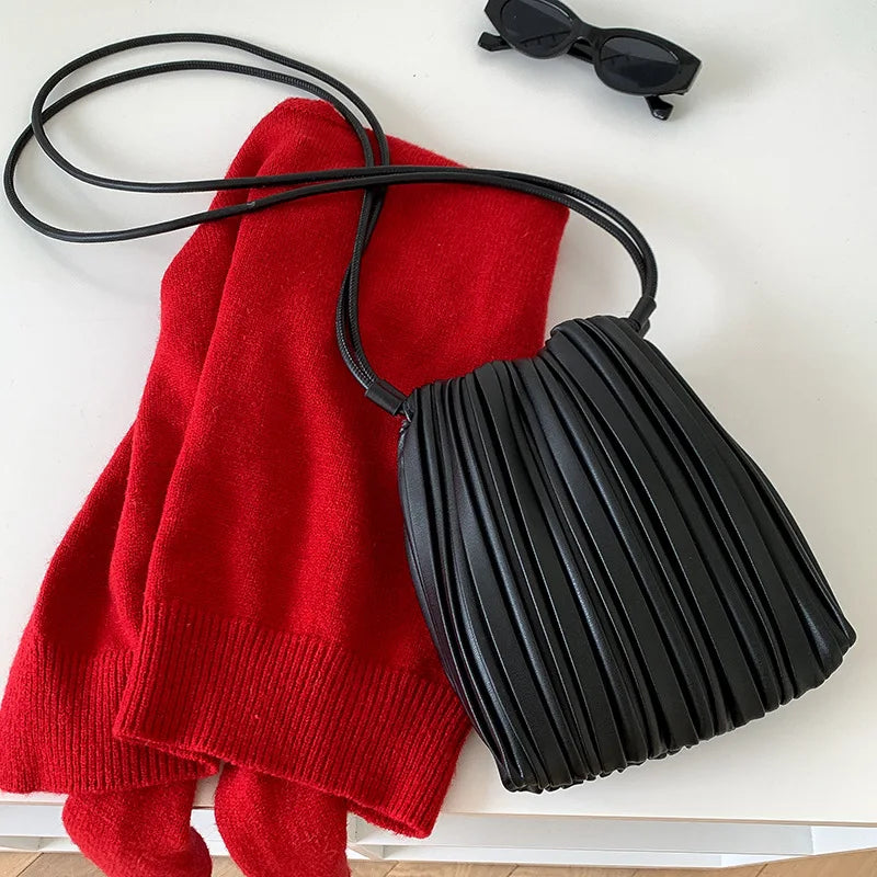 A red knitted sweater and a black pleated faux leather crossbody bag are displayed on a white surface.