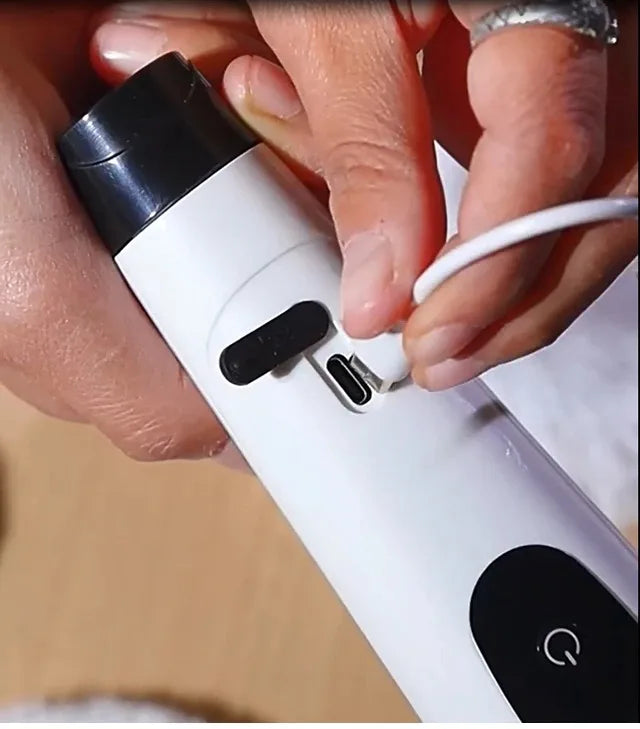 A hand is operating a white electric spin scrubber with interchangeable brush heads.