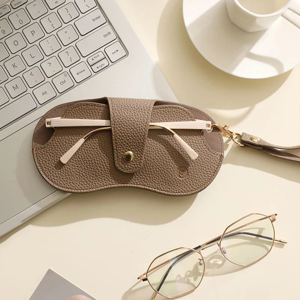 A tan PU leather glasses case with a retro lychee pattern is shown next to a laptop keyboard and eyeglasses.