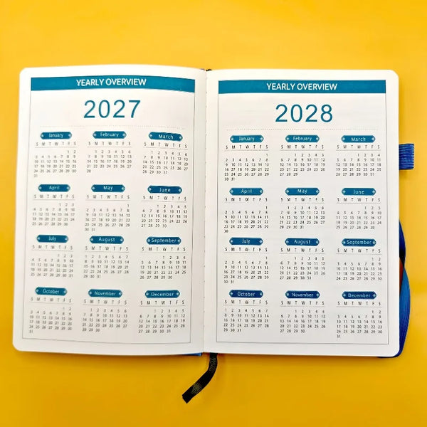Offener dreijähriger monatlicher Planer mit Jahresübersichten für 2027 und 2028 auf gelbem Hintergrund.