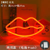 An orange neon sign shaped like lips is displayed on a red surface next to a book.
