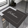 A dark gray bathroom mat with a white border is displayed on a glass surface.