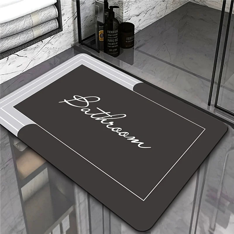 A dark gray bathroom mat with a white border is displayed on a glass surface.