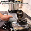A hand is using a gray scouring cloth to clean a black non-stick pan on a stovetop.
