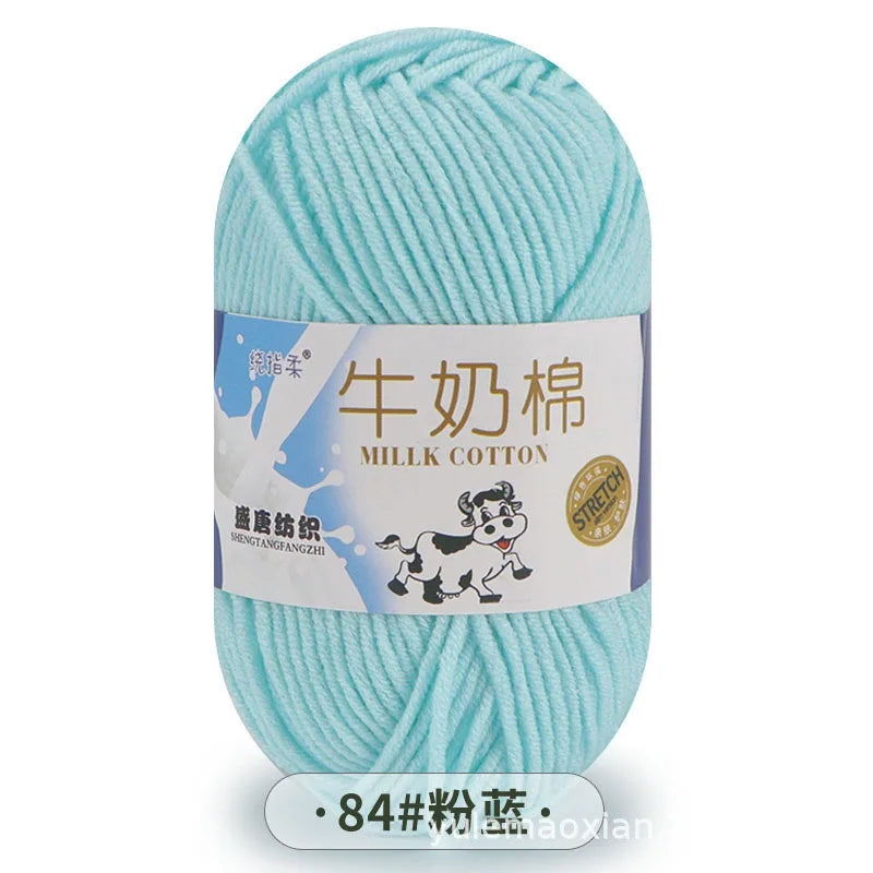 A ball of light blue milk cotton blend yarn with a label featuring a cow and text in Chinese and English.