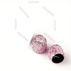 A close-up of pink crystal-cut tire valve caps with black cores.