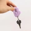 A hand holds a purple cloud-shaped retractable letter opener with a keychain loop attached.