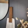 A rustic wooden wall-mounted towel clip is shown against a gray wall next to a mirror and a white towel.