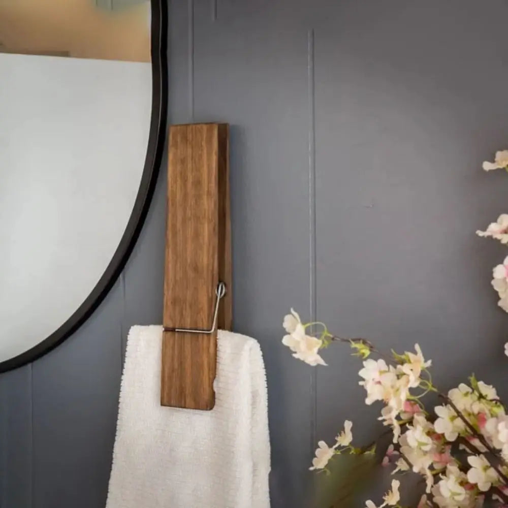 A rustic wooden wall-mounted towel clip is shown against a gray wall next to a mirror and a white towel.