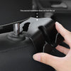 A hand is installing a black car headrest hook into a black leather handbag.