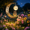 A solar owl garden light with moon decor illuminates a flower garden at night.