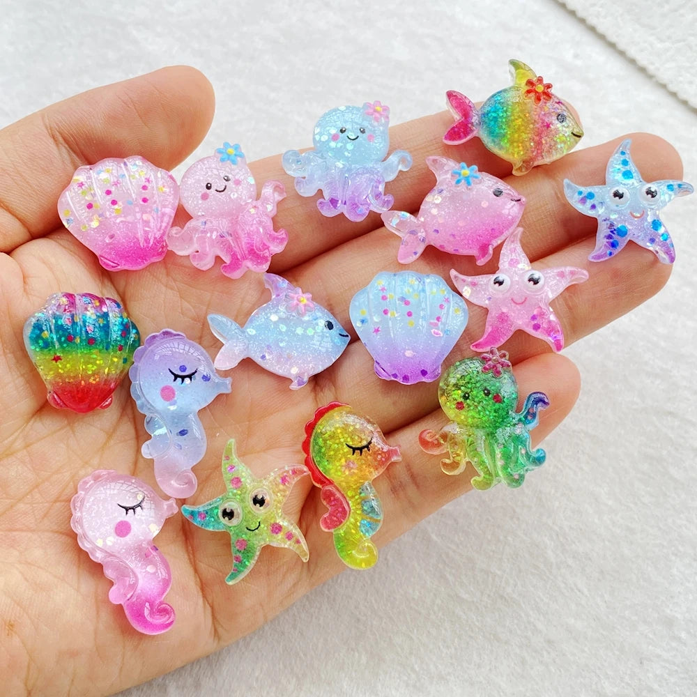 A hand holds a collection of colorful, iridescent resin charms shaped like fish and starfish for crafting.