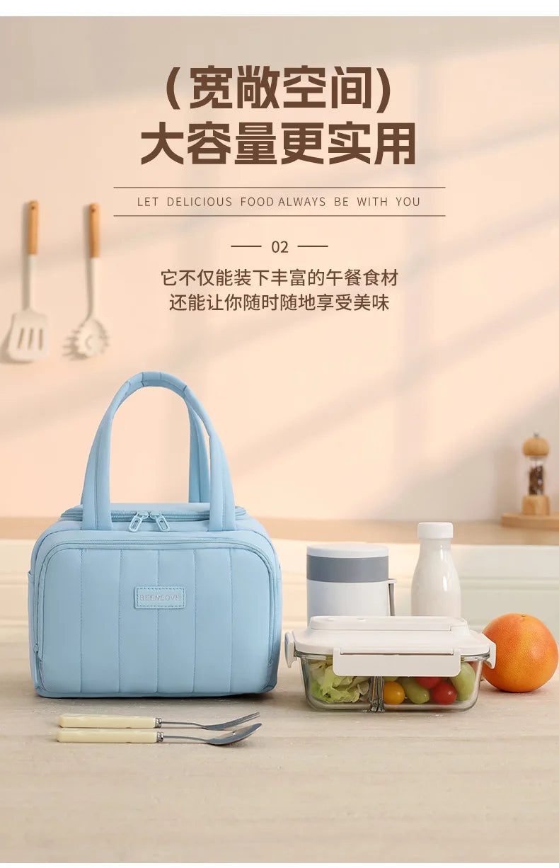 A light blue insulated quilted lunch tote bag is shown next to a clear food container on a wooden table.