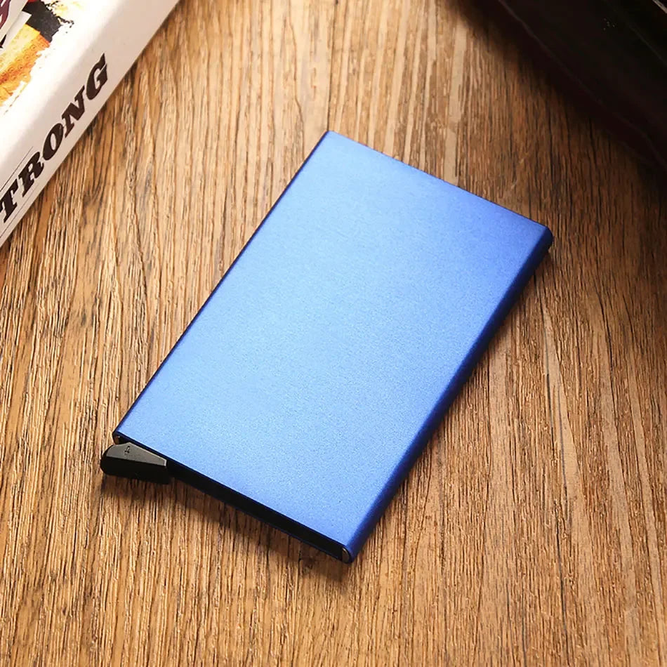 A blue slim metal RFID blocking card holder with a pop-up design resting on a wooden surface.