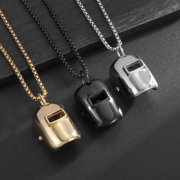 A set of stainless steel welder mask pendant necklaces in gold and silver tones displayed on a dark surface.