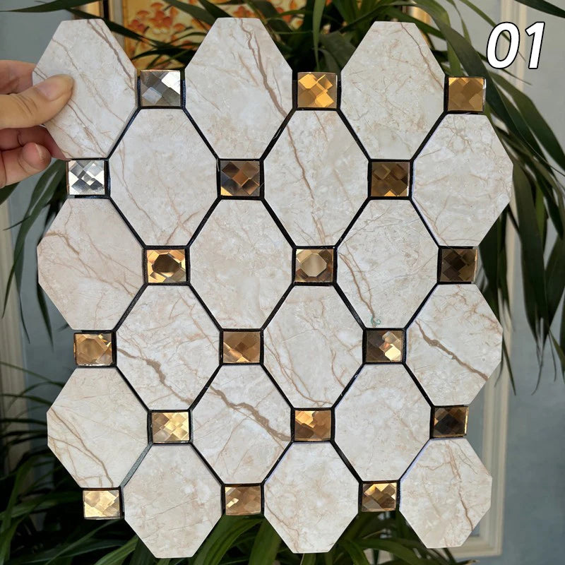 A hand holds a square mosaic tile featuring beige marble pattern and gold accents, set against green foliage.