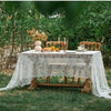 Elegant white lace tablecloth set up outdoors on a wooden table with floral decorations.