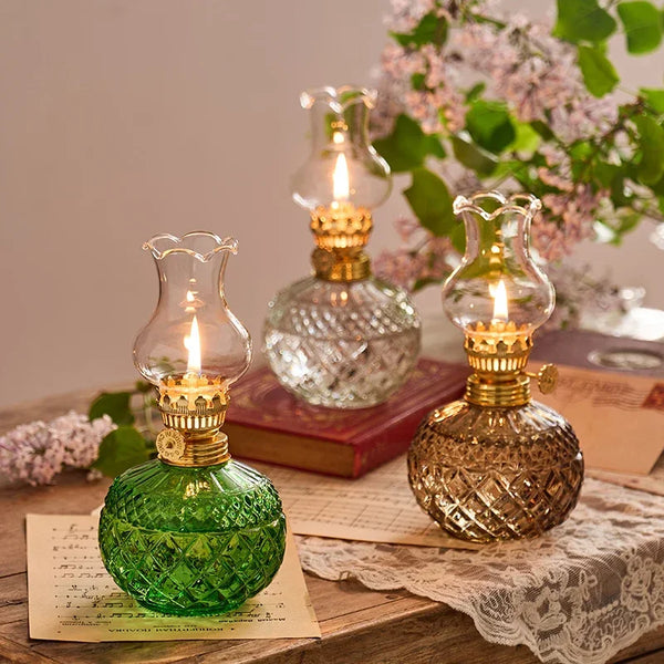 Une lampe à huile rustique vintage en verre vert repose sur une surface en bois à côté d'une pile de papier et de fleurs rose