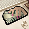 A hand is holding a stack of US dollar bills on a black non-slip bathroom rug.