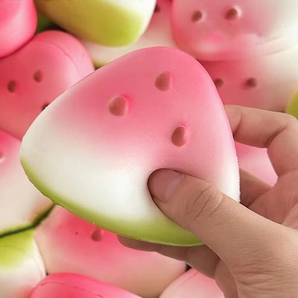 A hand holds a pink watermelon squishy fidget toy with green accents, showing its texture and shape.