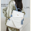 A woman is wearing a white leather backpack with blue accents and a satin green jacket.