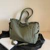 A olive green corduroy tote bag with a leather strap resting on a black surface next to a white book.