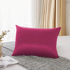 Une taie d'oreiller de soie magenta seule posée sur un tissu gris texturé près d'une fenêtre.