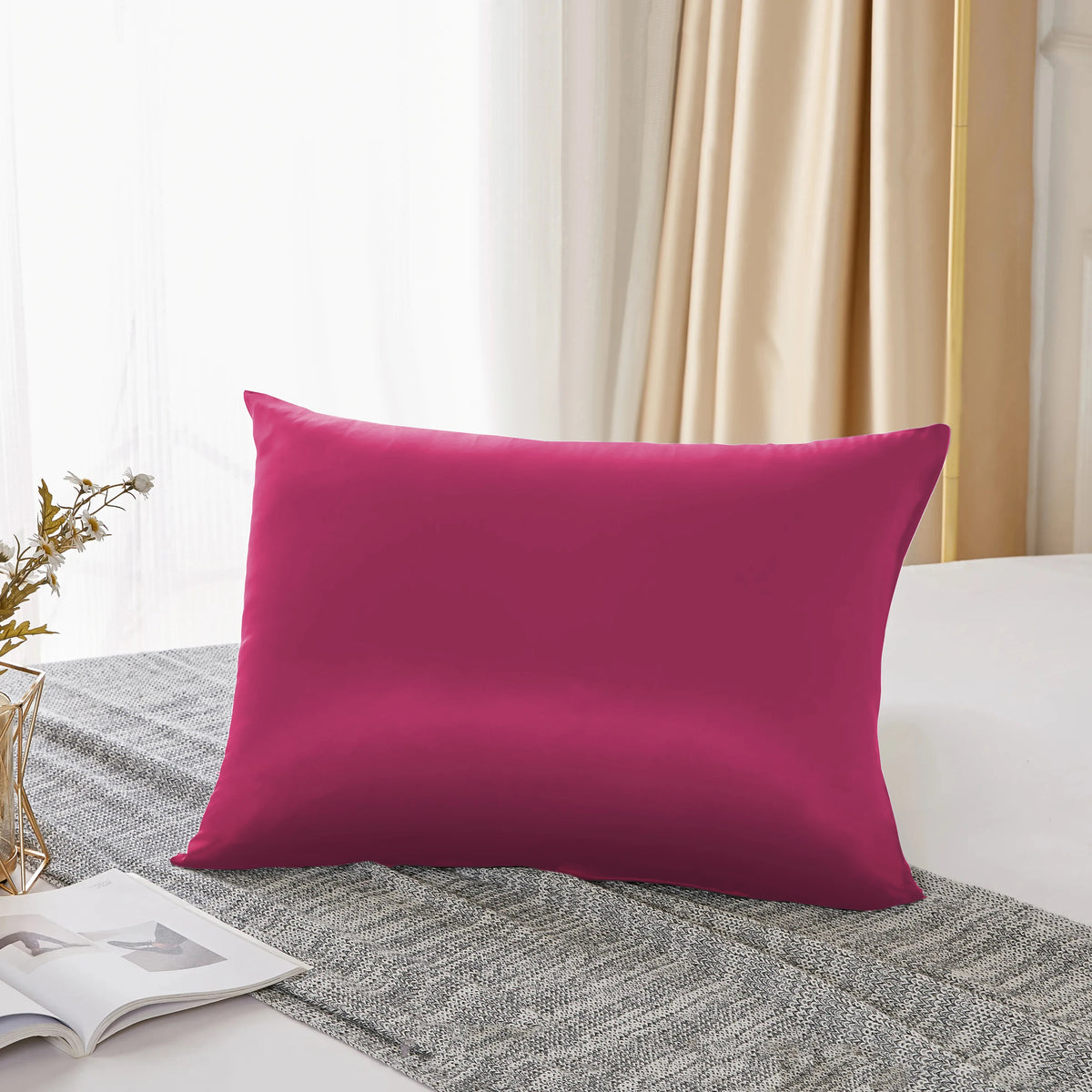 Une taie d'oreiller de soie magenta seule posée sur un tissu gris texturé près d'une fenêtre.