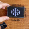 A black embroidered tactical patch featuring a white cross design on a wooden surface.