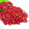 A pile of bright red tumbled crystal stone chips in a green bowl.