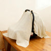 A beige breathable muslin cotton baby car seat cover draped over a wooden surface.