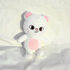 A white and pink fluffy cat plush doll with large eyes and a pink belly resting on a white surface.