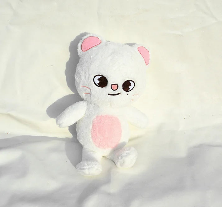 A white and pink fluffy cat plush doll with large eyes and a pink belly resting on a white surface.
