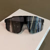 A pair of dark tinted sunglasses with a gradient blue and gray reflection resting on a white surface.