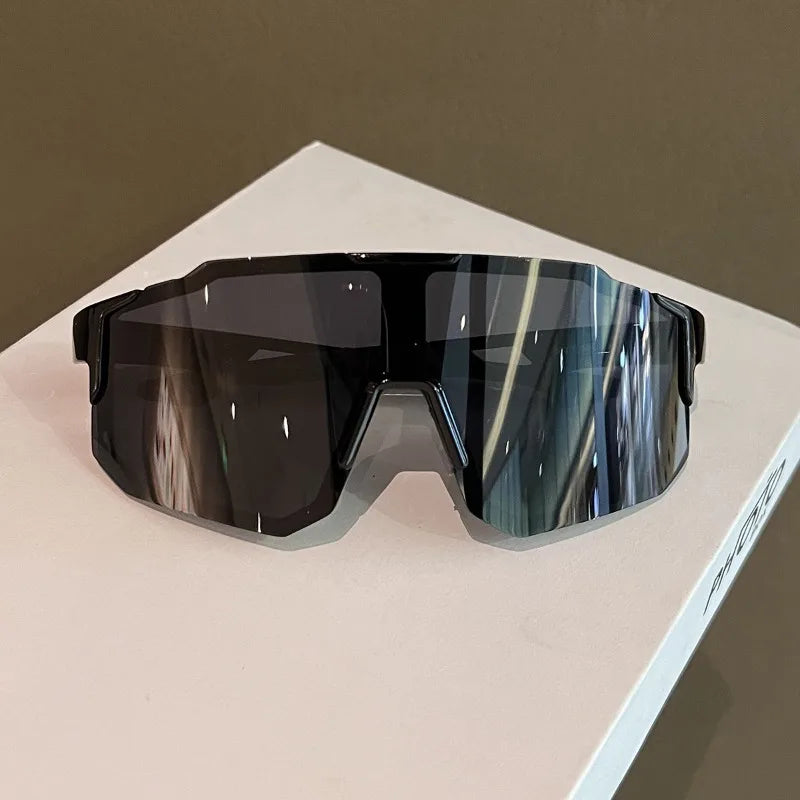 A pair of dark tinted sunglasses with a gradient blue and gray reflection resting on a white surface.