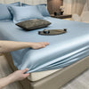 Un juego de sábanas ajustadas de algodón de lujo azul claro, drapeado sobre una cama, con almohadas y una pequeña bandeja vis