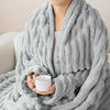 A person is wrapped in a soft gray brushed flannel throw blanket while holding a white mug.