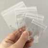 A hand holds several clear transparent PVC jewelry pouches with zip lock closures.