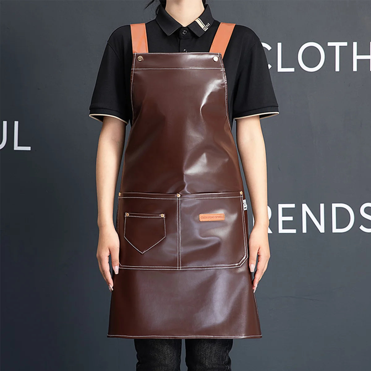 A woman wearing a brown PU leather multi-pocket kitchen apron with leather straps against a dark gray background.
