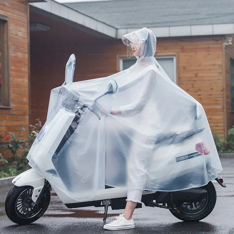 A person wearing a transparent waterproof motorcycle rain poncho is riding a white scooter outdoors.