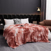 A cozy flannel fleece throw blanket with a tie-dye pattern draped over a bed in a modern bedroom.