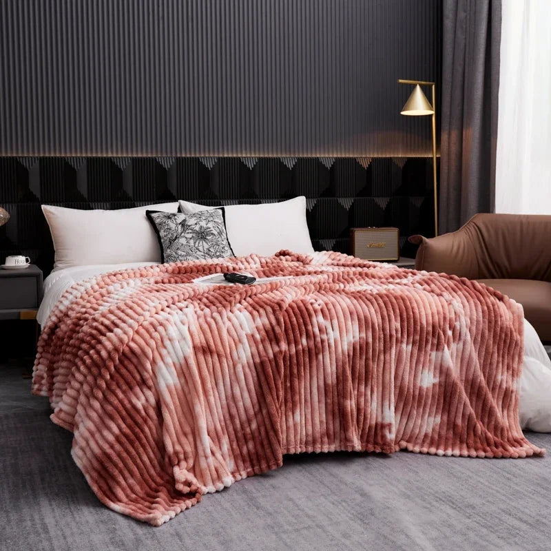 A cozy flannel fleece throw blanket with a tie-dye pattern draped over a bed in a modern bedroom.