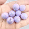 A hand holds several iridescent purple acrylic beads for jewelry making.