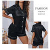 A woman models a black satin short suit consisting of a button-down top and matching shorts.