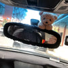 A plush teddy bear is placed on a car's rearview mirror.