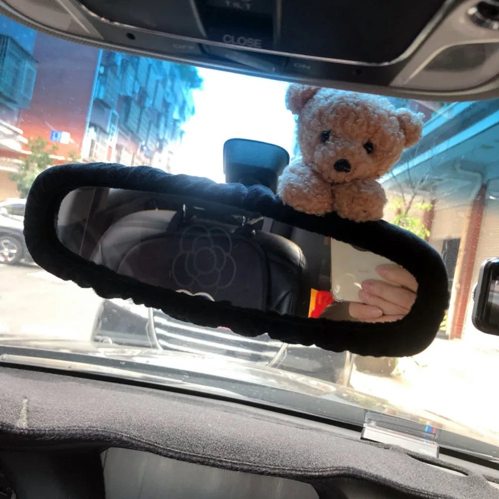 A plush teddy bear is placed on a car's rearview mirror.